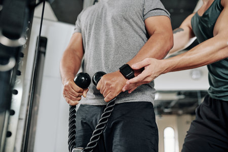 Close-up image of personal fitness trainer explaining client how to hold cable how to lift exercise...