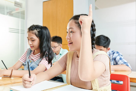 Smiling Vietnamese schoolgirl raising hand to ask question about the school test