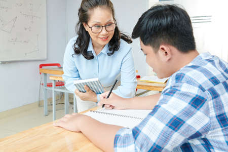 Smiling mature female math teacher helping student to solve equationの写真素材
