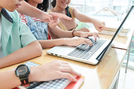 Cropped image of students gathered at laptop to work on school project togetherの写真素材