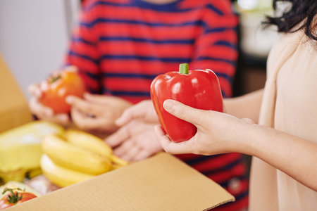 Close-up image of mature housewife taking vegetables out of cardboard box she ordered onlineの写真素材