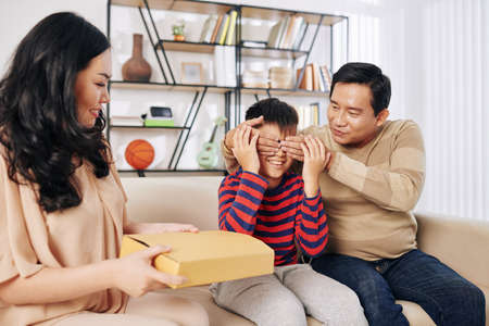 Father covering eyes of preteen son when mother giving him birthday presentの写真素材