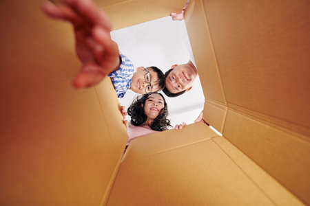 Cheerful Vietnamese mother, father and son looking inside cardboard box they received