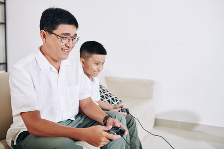 Mature Vietnamese man enjoying playing videogame with his preteen son at home