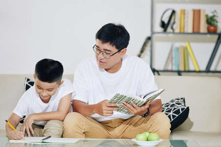Asian man controlling his preteen son solving equations when doing homeworkの写真素材