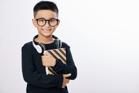 Positive Asian boy in glasses holding book and smiling at camera, isolated on whiteの写真素材