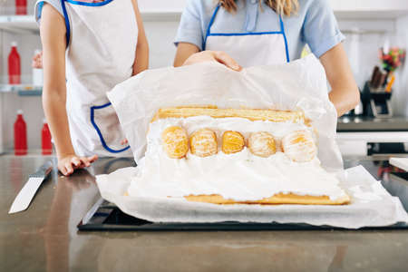 Housewife using paper sheet when making biscuit roll stuffed with sweet whipped cream and peeled tangerinesの写真素材