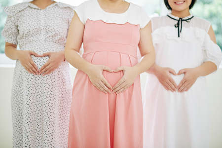 Cropped image of pregnant young woman in romantic dresses making heart shape hand sign on tummyの写真素材