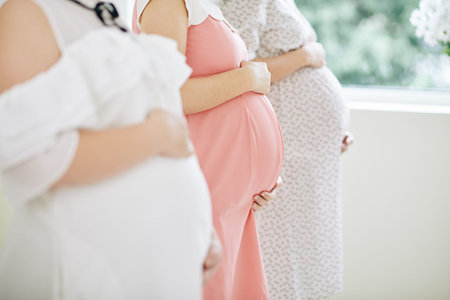 Group of pregnant women in beautiful dresses standing in row and touching their bellies