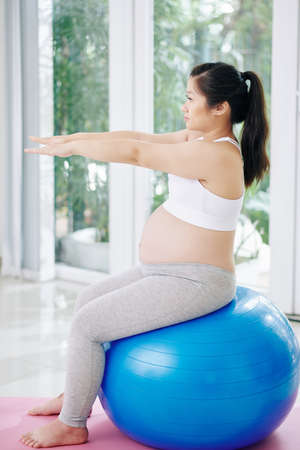 Pregnant Asian woman doing exercise on fitness ball at home in the morningの写真素材