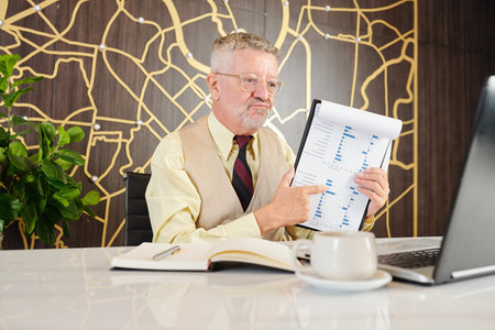 Unhappy aged businessman video calling department manager and showing sales report with poor figures