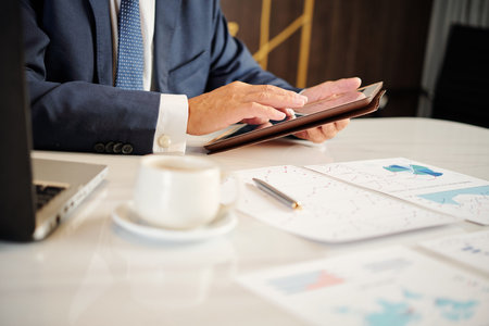 Businessman analyzing financial charts and checking important e-mails on tablet computer when having...
