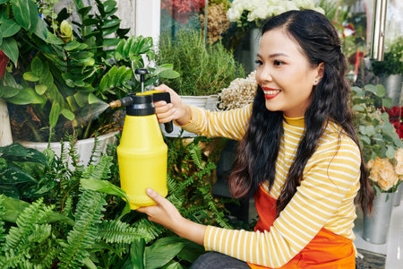 Pretty smiling young Asian florist spraying plants and flowers in her storeの写真素材