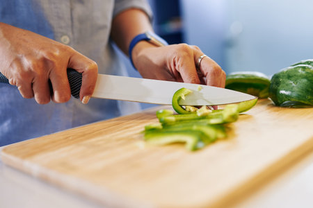 Close-up image of housewife cutting green bell pepper when making salad for dinnerの写真素材