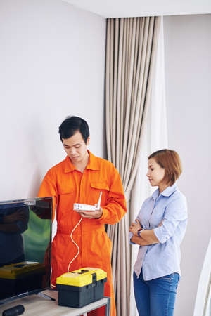 Serious housewife controlling technician installing wi-fi router in her roomの写真素材