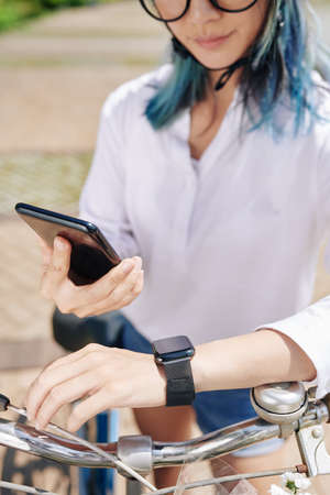 Young woman synchronizing smartphone and smartwatch before riding bicycle in ther cityの写真素材