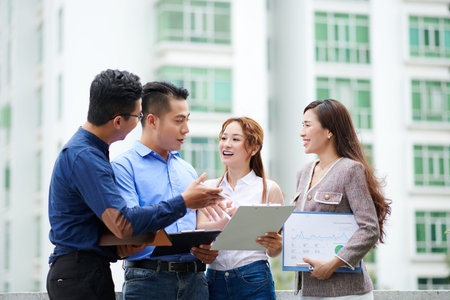 Positive young Vietnamese financial department managers discussing news and reports when standing...