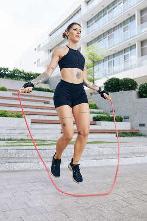 Fit young woman in short and sports bra jumping with skipping ropeの写真素材