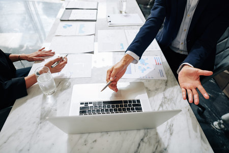 Hands of businessman showing report on laptop screen to female colleague at meeting