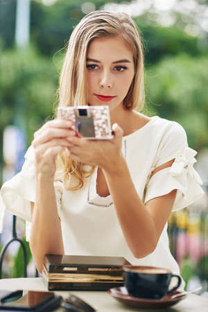 Attractive young blond woman looking at compact mirror to check her make-upの写真素材
