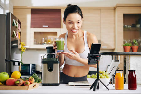 Smiling foof blogger video chatting with her subscribers and showing delicious fresh juice she made at homeの写真素材