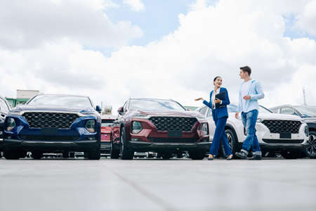 Positive female car dealership saleswoman walking along rows of new cars with customerの写真素材
