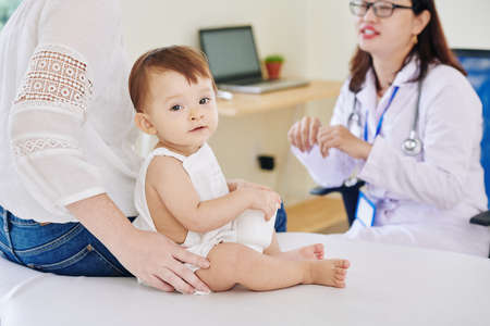 Cute little baby girl sitting on bed in office of pediatricianの写真素材