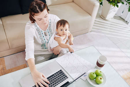 Little baby pointing at report of her mother working on laptop at home, view from aboveの写真素材
