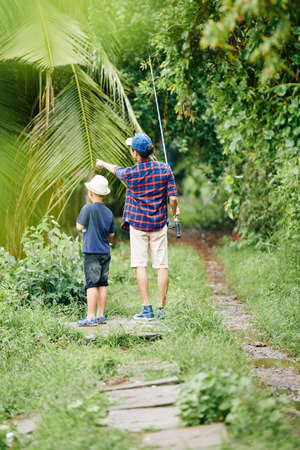 Father showing his son something interesting in forest when they are going to lake for fishingの写真素材