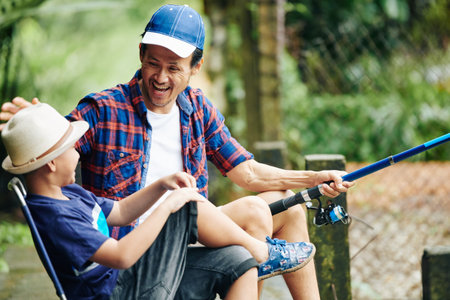 Happy laughing Asian father and son enjoying fishing together