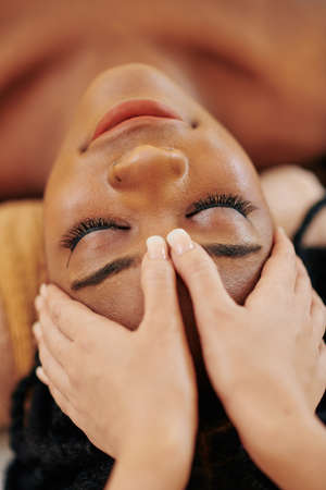 Close-up image of young African-American woman receiving professional head and face massage at spa salonの写真素材