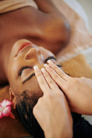 Close-up image of beautician massaging forehead of beautiful young Black womanの写真素材