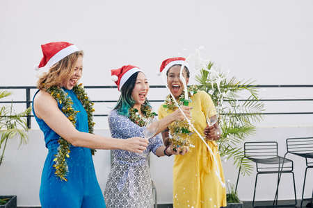 Group of joyful young women opening splashing champagne at Christmas party on rooftopの写真素材