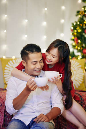 Happy beautiful young Vietnamese couple drinking delicious hot chocolate at homeの写真素材