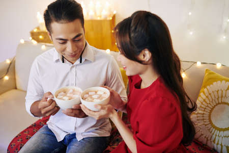 Smiling young Asian boyfriend and girlfriend drinking hot cocoa with marshmallowsの写真素材