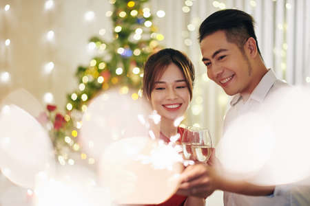 Beautiful happy smiling Vietnamese couple drinking champagne when celebrating Christmas at homeの写真素材