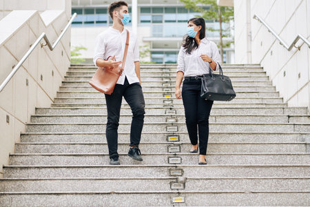 Multi-ethnic university students in protective masks walking down the stairs and discussing classes