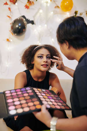 Pretty curly little girl looking at camera when artist applying her Halloween make-upの写真素材
