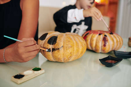 Children painting spooky faces on pumpkins when making decorations for Halloween partyの写真素材