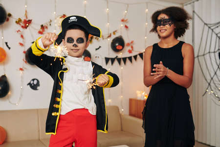 Teenage girl clapping to younger brother in pirate costume burning Bengal lights at Halloween partyの写真素材