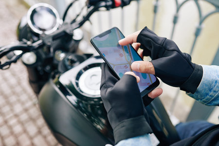 Hands of motorcyclist zooming in map on smartphone screen before riding to destination point