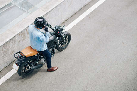 Man in denim jacket adjusting helmet and getting ready to ride on motorcycleの写真素材