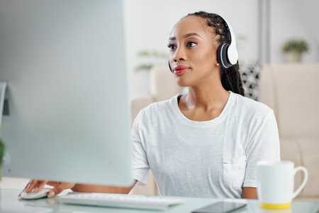 Portrait of pensive young Black woman with dreadlocks listening to music when working on computer