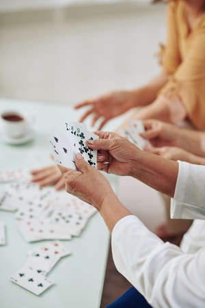 Hands of senior women playing cards and drinking tea when spending weeend togetherの写真素材