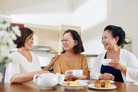 Group of happy senior women drinking tea, eating cakes and discussing news at homeの写真素材