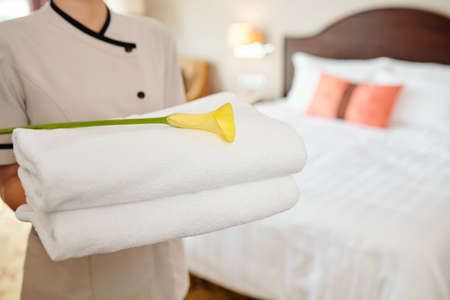 Hotel maid holding stack of fluffy white towels with yellow calla lilyの写真素材