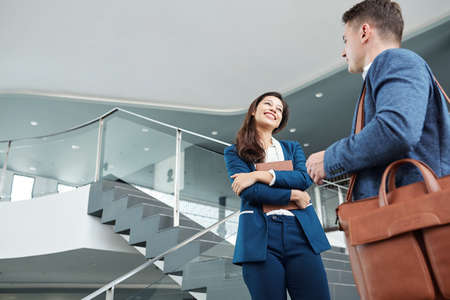 Attractive smiling young business lady talking to colleague in office hallの写真素材