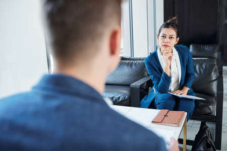 Pensive young businesswoman listening to ideas of her colleague at meetingの写真素材