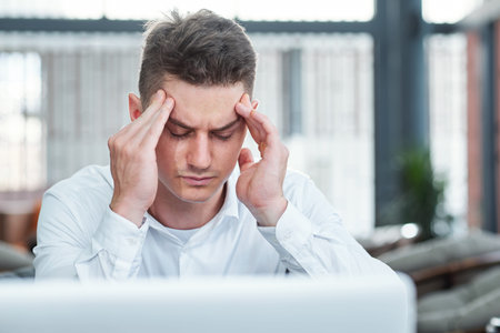 Young businessman having headache after working on laptop all day long