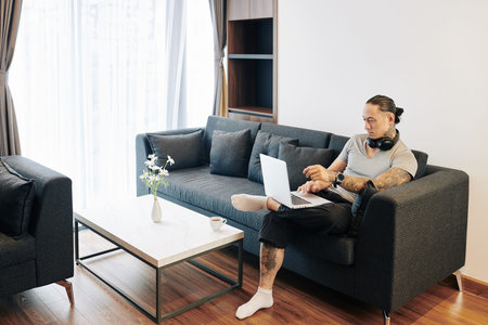 Handosme fit man sitting on sofa at home and answering e-mail or programming on laptop